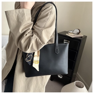 Close-up of black leather tote bag with elegant silk scarf detail on handle for daily commute