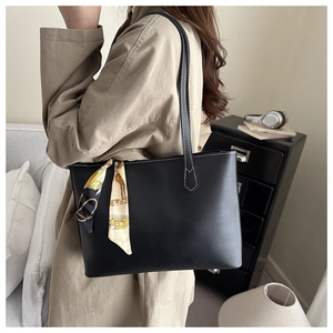 Black tote bag with white stitching and decorative yellow silk scarf on a model