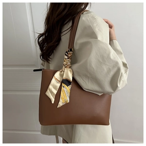 Detail of a brown leather tote bag handle featuring a decorative printed silk scarf accent