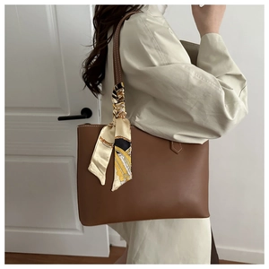 Close-up of brown tote bag featuring decorative silk scarf handle and white stitching detail