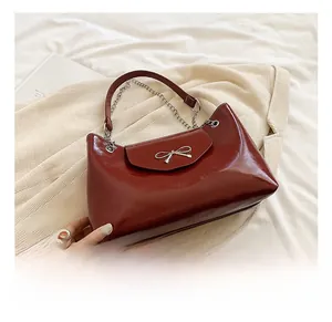Detail of burgundy patent leather tote with silver bow hardware and chain strap