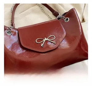 Detailed close-up of glossy wine red leather tote bag with silver bow hardware buckle