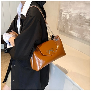 Detail of caramel leather crescent bag featuring a metallic bow clasp and chain strap