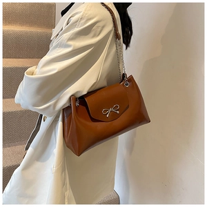 Brown leather tote with silver bow detail and chain strap worn with beige trench coat