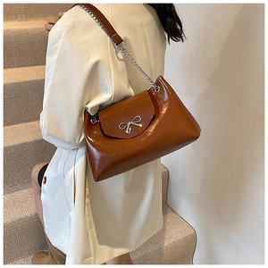 Detail of a brown leather shoulder bag featuring a silver bow buckle and chain strap