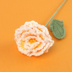 Detail of handcrafted crochet peony with gradient petals and green leaves on orange background