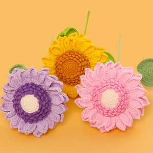 Detail of three handmade crochet sunflowers in purple, yellow and pink on orange background