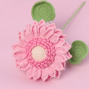 Close-up of pink handmade crochet sunflower with green leaves and knitted texture