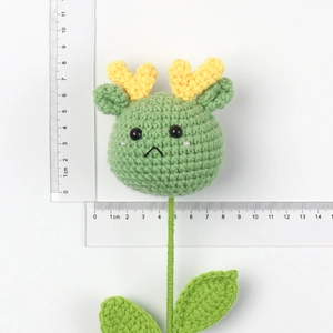 Detail of green handmade crochet doll featuring yellow horns and detailed leaf stem