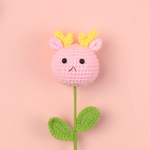 Close-up of handmade crochet dragon flower doll with pink yarn texture and green leaves