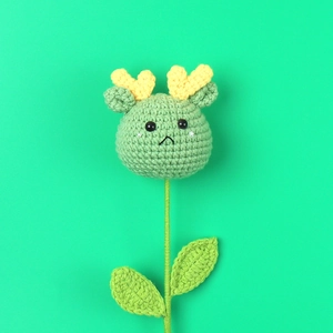 Detail of a handmade green knitted animal flower with yellow horns and leaf stem