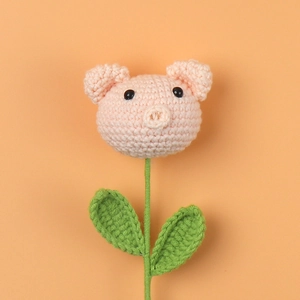 Close-up of handmade crochet pink pig flower with green leaves on orange background