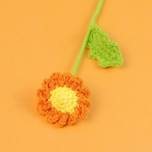 Close-up of handmade crochet daisy with orange petals and detailed green leaf texture