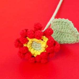 Gros plan d'un gerbera fait main au crochet avec pétales rouges et tige verte sur fond rouge