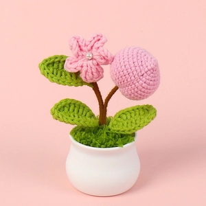 Detail of handmade crochet potted plant with pink flower and knitted fruit on moss base