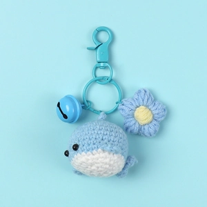 Detail of handmade crochet blue whale keychain with knitted flower and metal bell