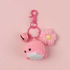 Handmade pink crochet dolphin keychain with flower charm and bell on pink background