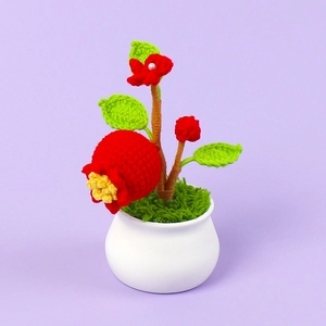 Macro detail of handmade crochet red pomegranate potted plant in a white ceramic base
