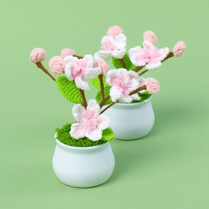 Handmade crochet peach blossom potted plants with green leaves on a soft green background