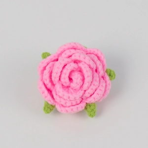 Detail of a handmade pink crochet rose with green leaves crafted from soft cotton yarn