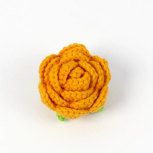 Close-up of handmade crochet orange rose with green leaves showing soft yarn texture