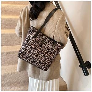 Detail of leopard print tote bag with gold metal logo worn by a model in a beige suit