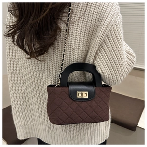 Détail du sac matelassé marron foncé avec fermoir doré sur un pull en maille beige