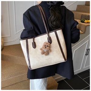 Détail d'un grand sac cabas beige avec anses marron et accessoire ours en peluche