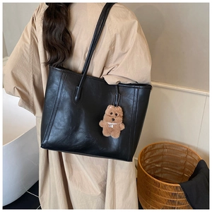 Detail of black leather tote bag with shoulder straps and brown plush bear charm