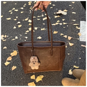 Detail of dark brown leather tote bag with a cute plush puppy pendant on fallen ginkgo leaves