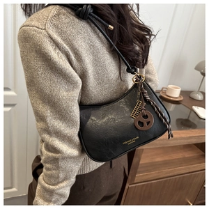 Detail of black leather crescent shoulder bag with golden text and unique charms
