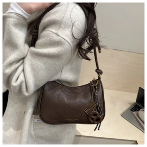 Detail of dark brown semi-moon shoulder bag with knot strap and golden charms