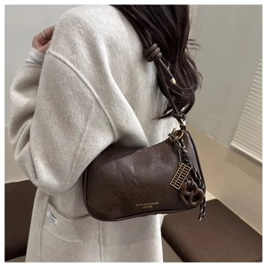 Detail of dark brown leather underarm bag with knot strap and decorative metal charms