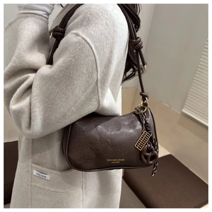 Close-up of deep brown oil wax leather shoulder bag with gold logo and heart charm
