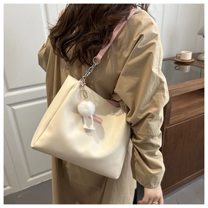 Detail of off-white tote bag with pink straps, chain accents, and a fluffy pompom charm