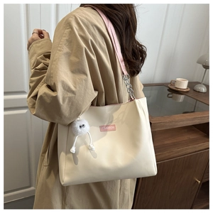Detail of cream white tote bag with pink label and plush charm in cozy interior