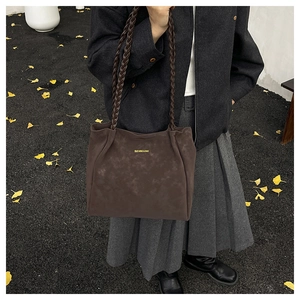 Close-up of deep brown suede tote bag with golden lettering and braided long handles