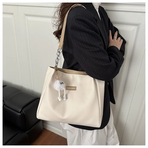 Detail of cream tote bag featuring fashion tag and plush charm on a suit-clad model