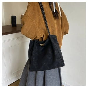 Detail of a black matte tote bag with woven shoulder strap shown on a model