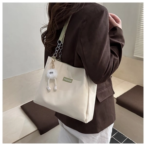 Close-up of cream tote bag with green FASHION label and plush monster pendant detail