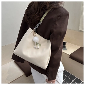 Detail of beige leather tote bag with green strap chain and plush pompom keychain accessory