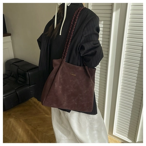 Detail of burgundy faux suede tote bag featuring braided shoulder straps and gold lettering