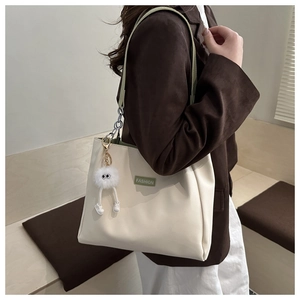 Detail view of cream tote bag with green straps and cute white plush doll charm