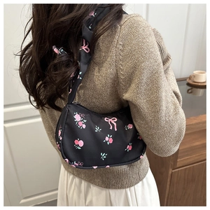 Detail of black pleated underarm bag with pink rose and bow prints worn by a model