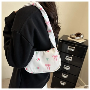 Detail of floral underarm bag with pink bow pattern on white canvas worn by model
