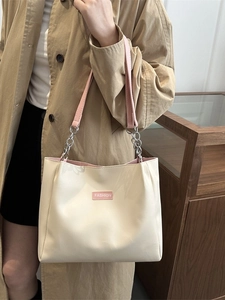 Minimalist beige tote bag with pink straps and fashion label shown on model with trench coat
