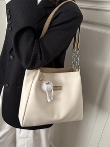 Beige faux leather tote bag with chain strap and plush charm worn by a model