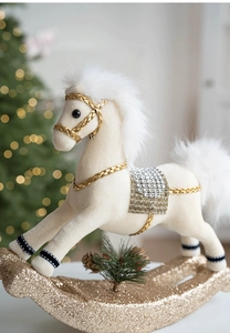 Detail of white plush rocking horse ornament with gold glitter base and festive pine cone
