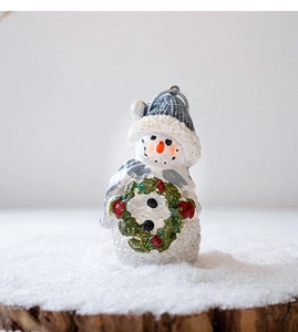 Close-up of resin Christmas snowman in blue hat with garland on snowy wood base