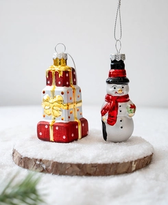 Detailed view of hand-painted glass snowman and gift box Christmas ornaments on snow